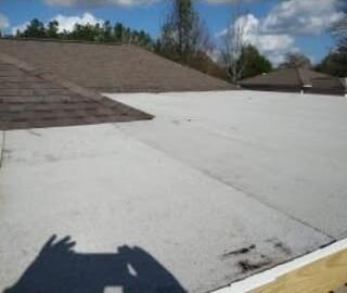 Low-slope roof section meeting a brown shingled roof under a blue sky