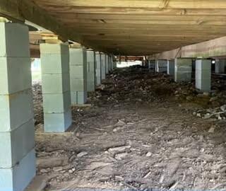 Long row of new gray concrete block piers under a house's floor framing in a dirt crawl space