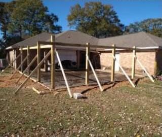 Wood porch frame with temporary braces going up along the back of a brick ranch house